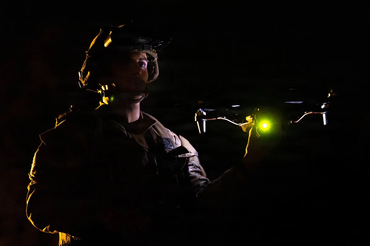 A soldier launching a small quadcopter drone at night.