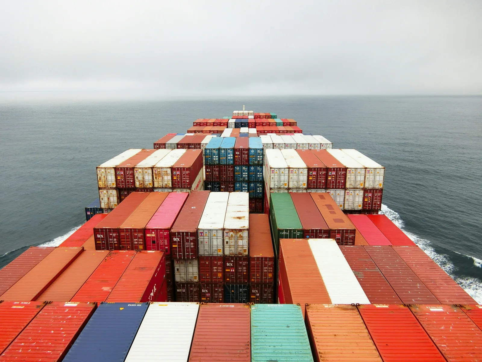 The view forward from a container ship’s bridge, deck stacked with containers, underway on open sea.