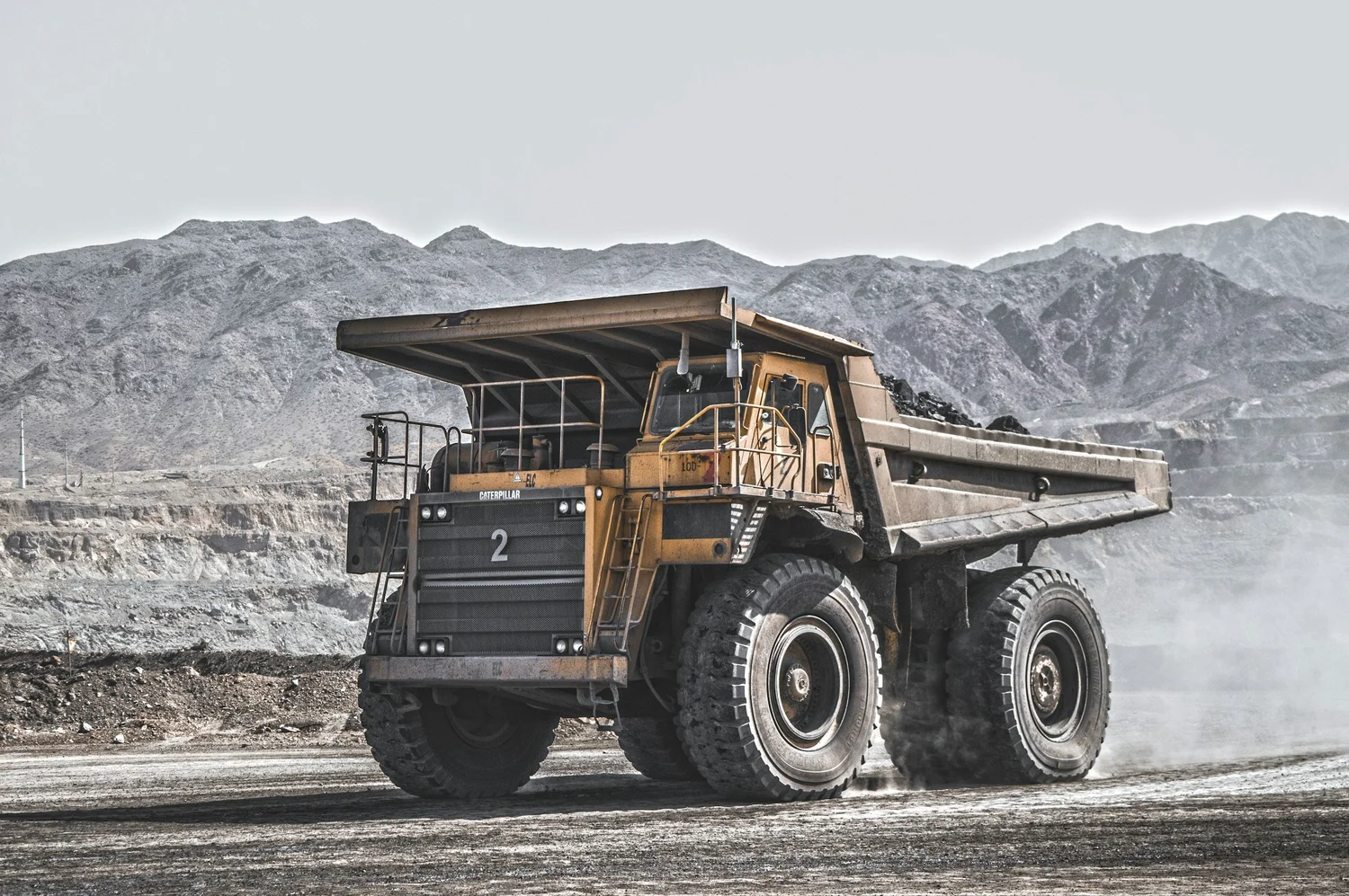 A large mining haul truck on a mine haul road below mountains.