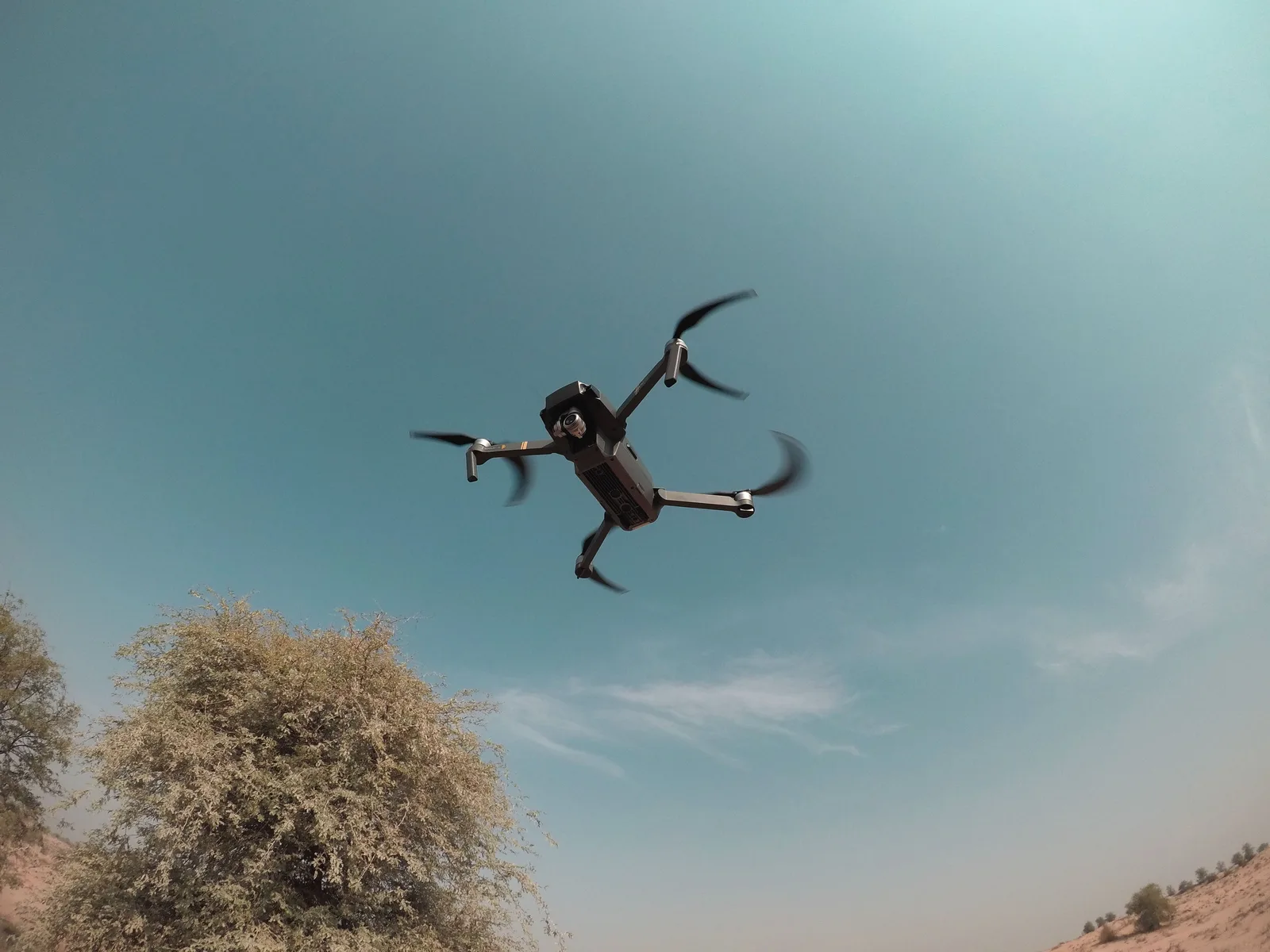 A quadcopter drone in flight over arid terrain.