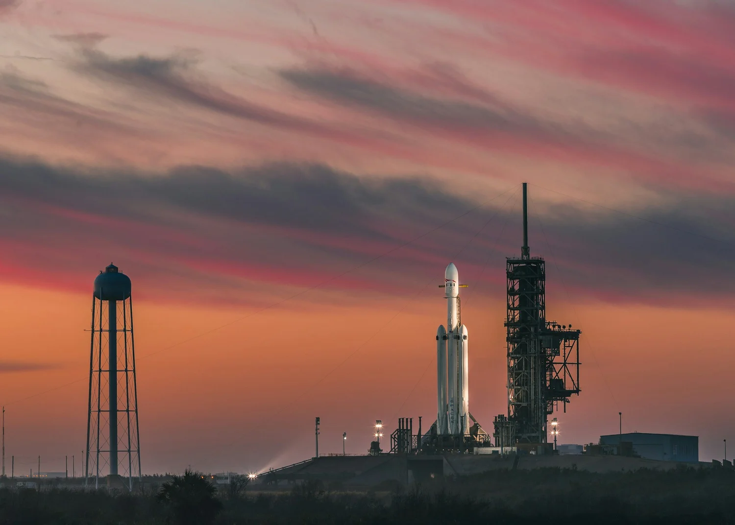 A heavy-lift rocket standing on the launch pad at sunset.