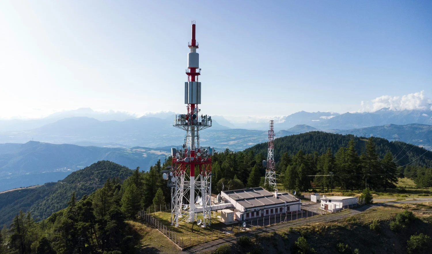 A red-and-white communications tower on a mountain summit above forested ranges.